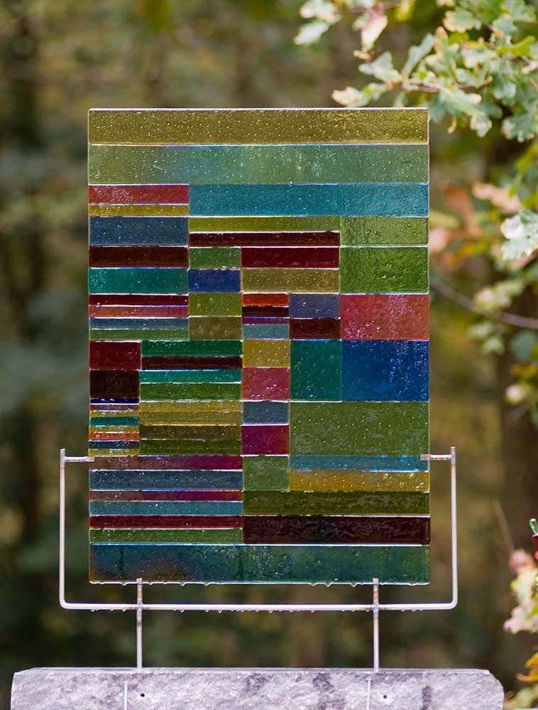 Glaskunstwerk met horizontale stroken gekleurd glas, in de tuin
